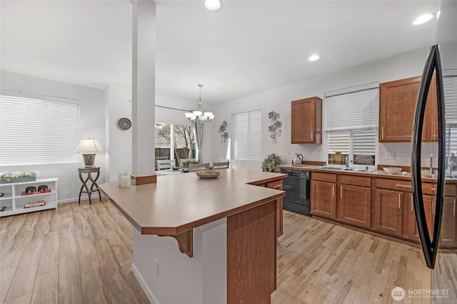 kitchen with a center island, black dishwasher, brown cabinets, light wood finished floors, and a sink