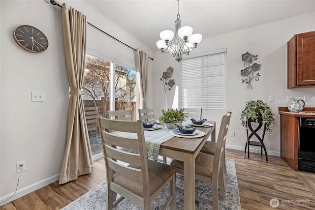 dining room with light wood-type flooring, baseboards, and an inviting chandelier