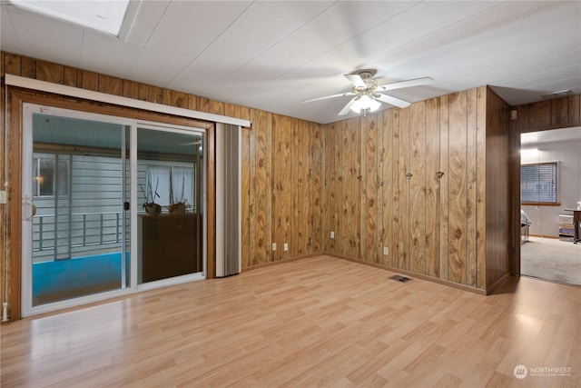 empty room with wooden walls, ceiling fan, and light wood-type flooring