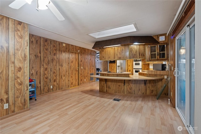 kitchen featuring stainless steel fridge with ice dispenser, wood walls, light hardwood / wood-style floors, and kitchen peninsula