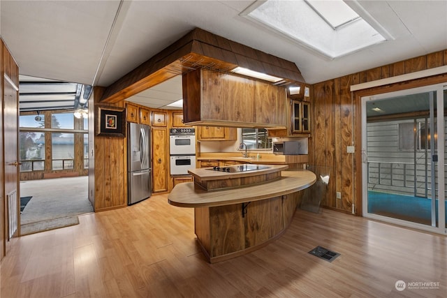 kitchen featuring stainless steel fridge, white double oven, black electric stovetop, kitchen peninsula, and wood walls