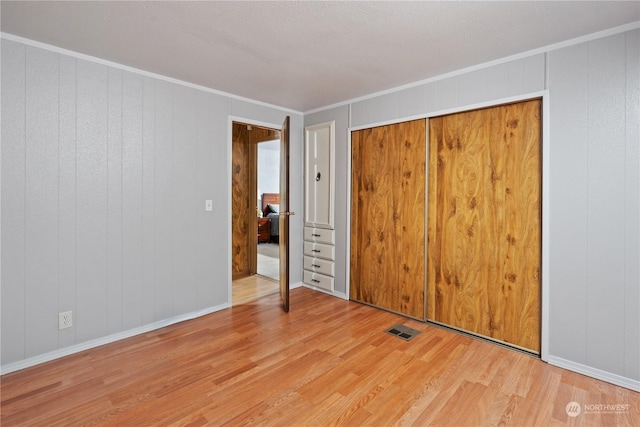 unfurnished bedroom featuring ornamental molding, a closet, and light wood-type flooring