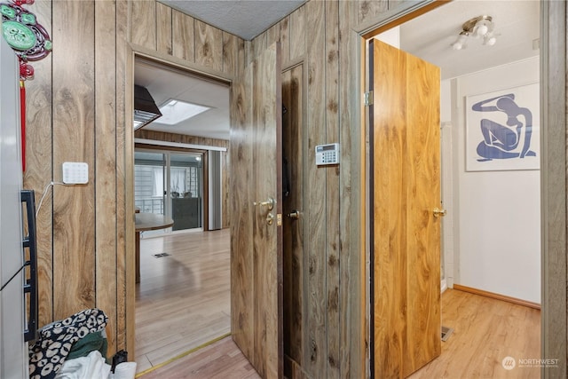 hall with a skylight, wooden walls, and light wood-type flooring