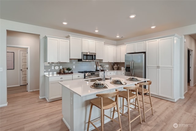 kitchen with a kitchen island with sink, sink, white cabinetry, and appliances with stainless steel finishes