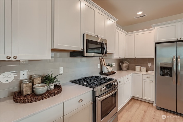 kitchen with stainless steel appliances, white cabinets, light wood-type flooring, and decorative backsplash