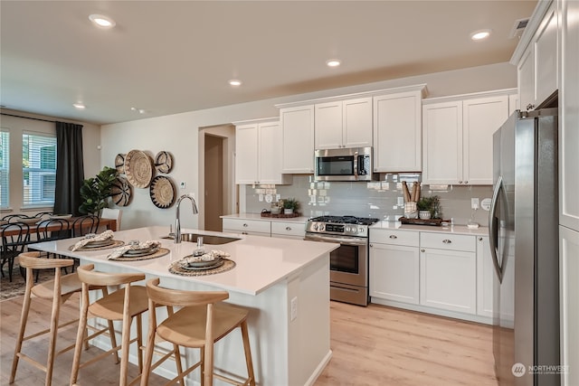 kitchen featuring a breakfast bar, sink, white cabinetry, appliances with stainless steel finishes, and an island with sink