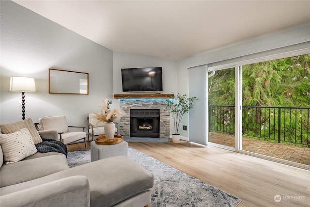 living room featuring hardwood / wood-style flooring, vaulted ceiling, and a stone fireplace