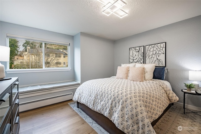 bedroom with a baseboard heating unit, light hardwood / wood-style flooring, and a textured ceiling