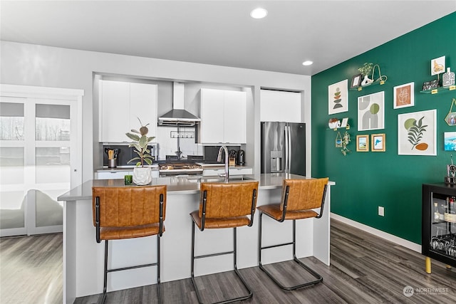 kitchen featuring white cabinetry, sink, a breakfast bar area, stainless steel refrigerator with ice dispenser, and wall chimney exhaust hood