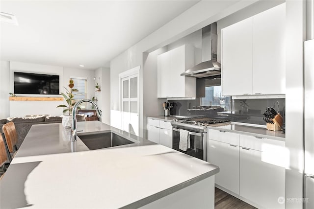 kitchen featuring sink, white cabinetry, stainless steel gas range oven, decorative backsplash, and wall chimney exhaust hood