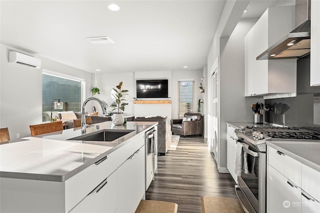 kitchen with sink, a kitchen island with sink, stainless steel appliances, a wall unit AC, and wall chimney exhaust hood