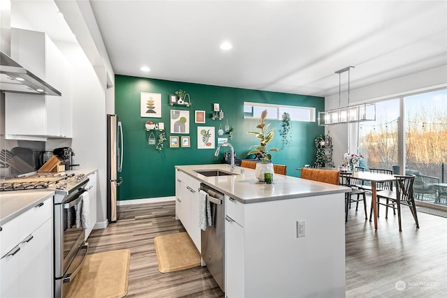 kitchen with sink, a kitchen island with sink, hanging light fixtures, white cabinets, and wall chimney exhaust hood