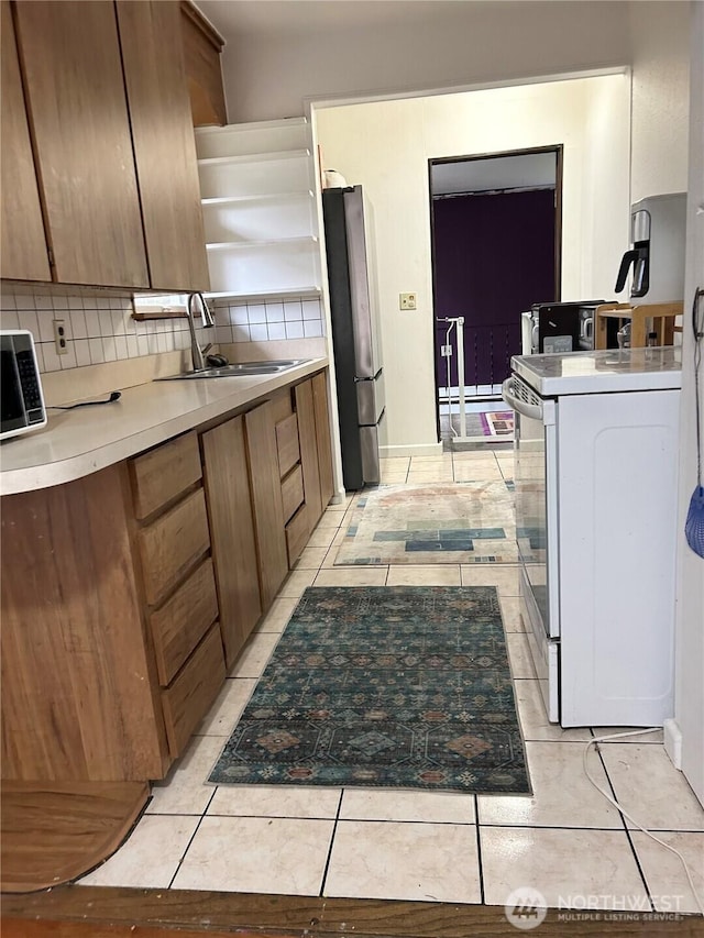 kitchen with white electric range, a sink, backsplash, freestanding refrigerator, and brown cabinetry