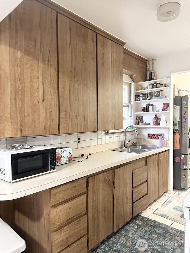 kitchen featuring light tile patterned floors, tasteful backsplash, light countertops, freestanding refrigerator, and a sink