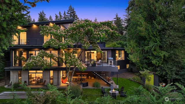 back house at dusk featuring a balcony and a patio area