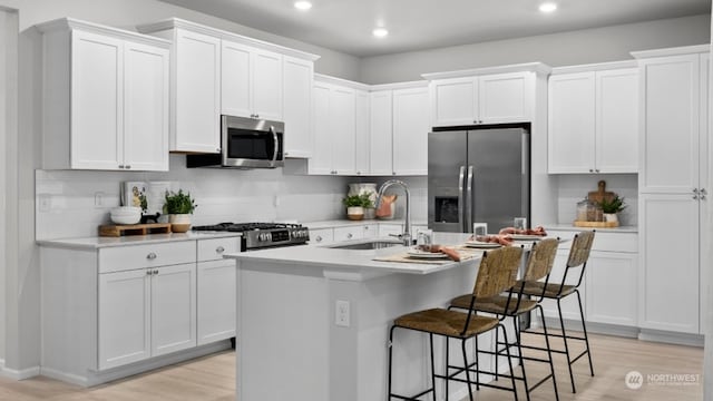 kitchen featuring sink, a breakfast bar area, white cabinetry, appliances with stainless steel finishes, and a kitchen island with sink