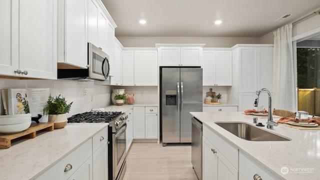 kitchen with sink, light stone counters, light hardwood / wood-style flooring, appliances with stainless steel finishes, and white cabinets