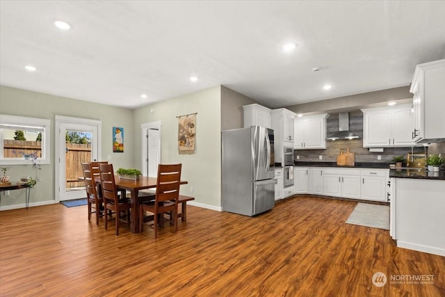 kitchen with tasteful backsplash, appliances with stainless steel finishes, dark hardwood / wood-style flooring, wall chimney range hood, and white cabinets