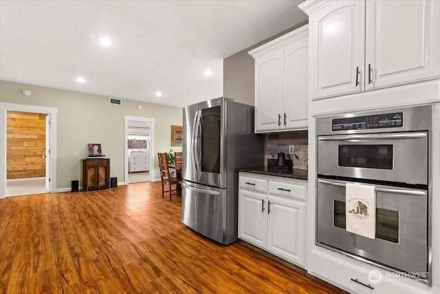 kitchen with stainless steel appliances, white cabinetry, backsplash, and dark hardwood / wood-style flooring