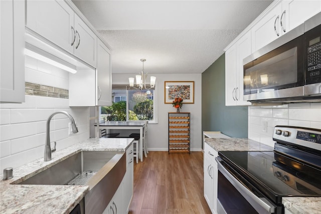 kitchen featuring pendant lighting, sink, white cabinets, light stone counters, and stainless steel appliances