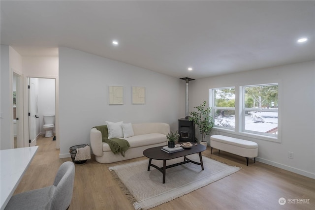 living room with lofted ceiling, a wood stove, and light wood-type flooring