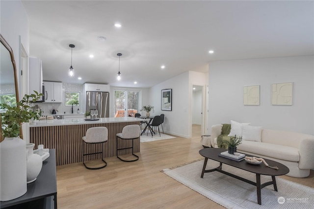 living room featuring vaulted ceiling, sink, and light wood-type flooring