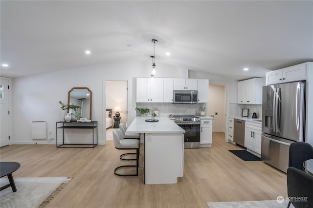 kitchen with pendant lighting, white cabinets, a kitchen bar, stainless steel appliances, and light hardwood / wood-style flooring