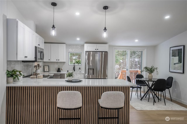 kitchen with white cabinetry, hanging light fixtures, light wood-type flooring, kitchen peninsula, and stainless steel appliances