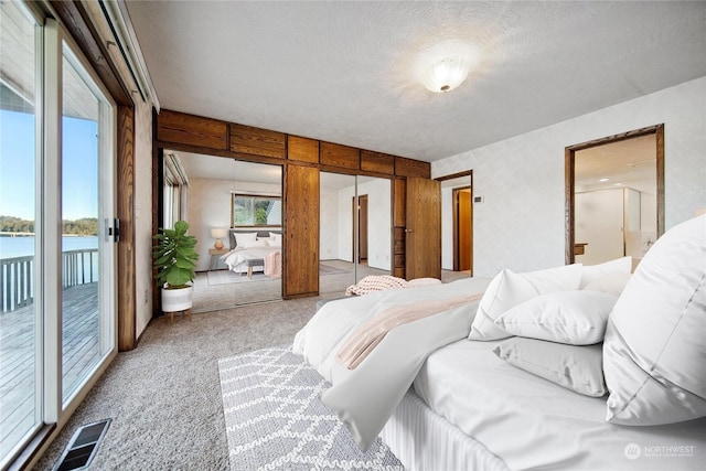 bedroom with carpet flooring, access to outside, a textured ceiling, and a water view