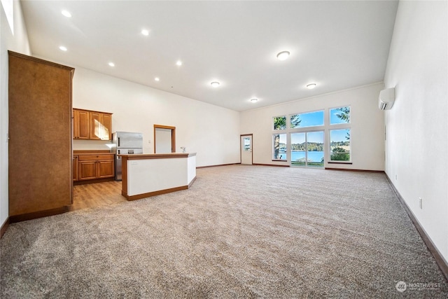 unfurnished living room featuring light carpet, a high ceiling, a wall mounted AC, and a water view