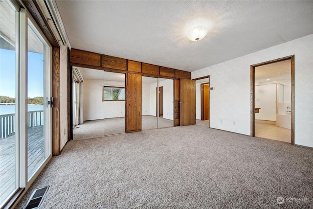 unfurnished bedroom featuring ensuite bathroom, a water view, a textured ceiling, light carpet, and access to outside