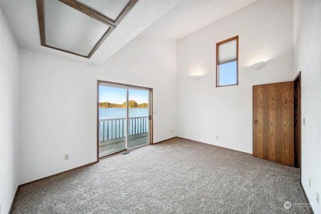 carpeted empty room with a water view, high vaulted ceiling, and a wealth of natural light