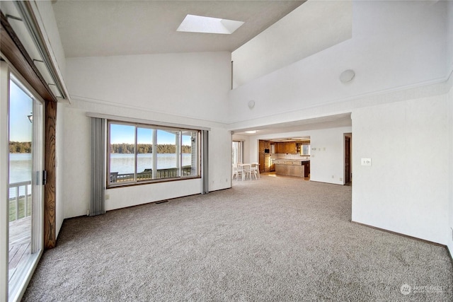 unfurnished living room with a skylight, carpet floors, high vaulted ceiling, and a water view