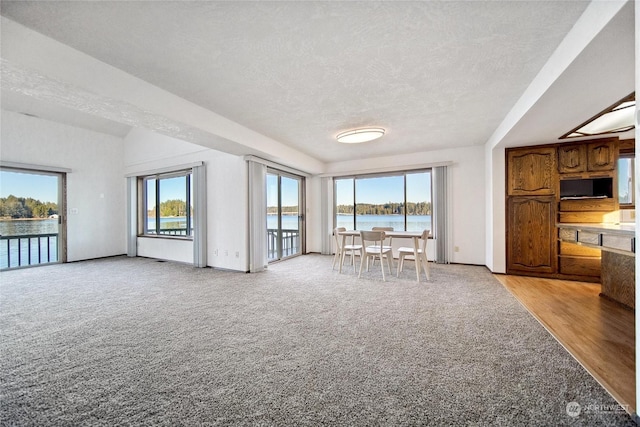 unfurnished living room featuring a water view, a wealth of natural light, and light carpet