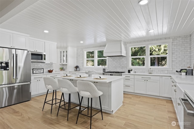 kitchen featuring appliances with stainless steel finishes, a kitchen island, custom range hood, and white cabinets