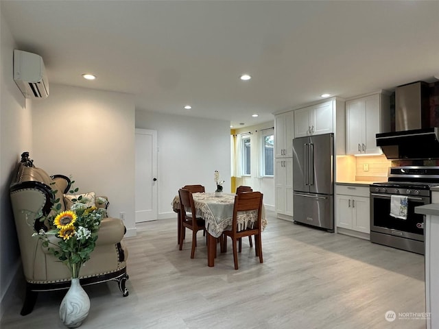 kitchen featuring white cabinetry, light wood-type flooring, appliances with stainless steel finishes, a wall unit AC, and wall chimney range hood