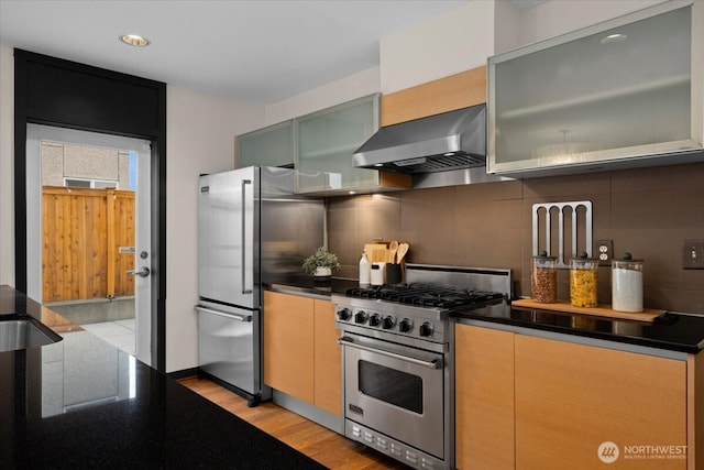 kitchen with wall chimney exhaust hood, backsplash, light wood-style flooring, and stainless steel appliances