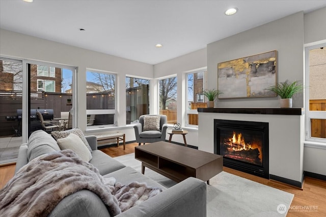 living area featuring baseboards, wood finished floors, a glass covered fireplace, and recessed lighting