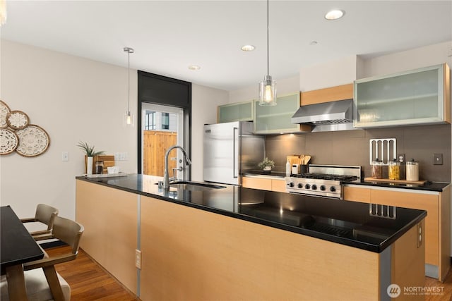 kitchen with stainless steel appliances, wall chimney range hood, dark countertops, and a sink