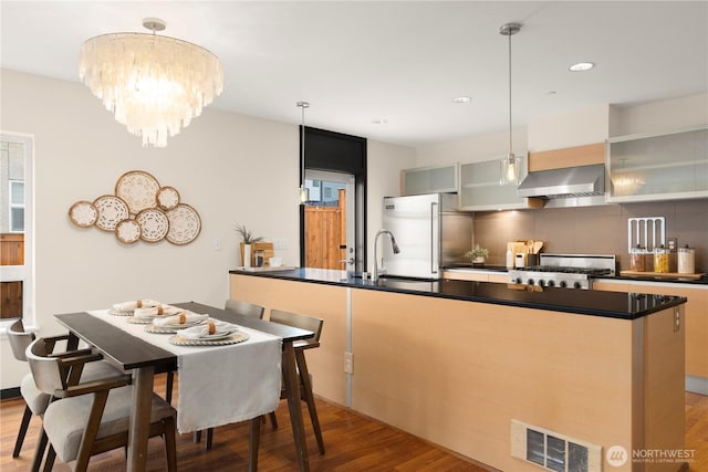 kitchen featuring built in fridge, a sink, visible vents, wall chimney exhaust hood, and dark countertops