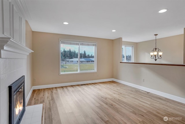 unfurnished living room with an inviting chandelier, a tiled fireplace, and light wood-type flooring