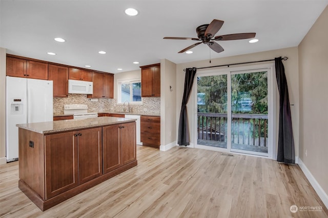 kitchen with sink, tasteful backsplash, light stone counters, a center island, and white appliances