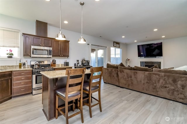 kitchen with appliances with stainless steel finishes, pendant lighting, a kitchen breakfast bar, light stone counters, and light hardwood / wood-style flooring