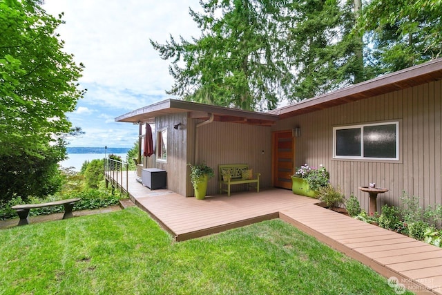 rear view of property featuring a deck with water view and a lawn