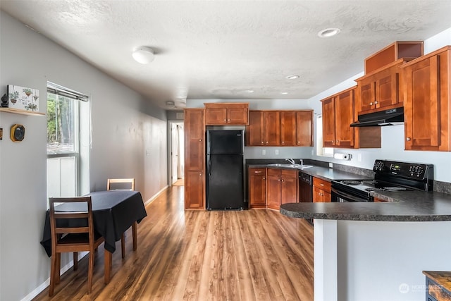 kitchen featuring sink, light hardwood / wood-style flooring, black appliances, and a textured ceiling