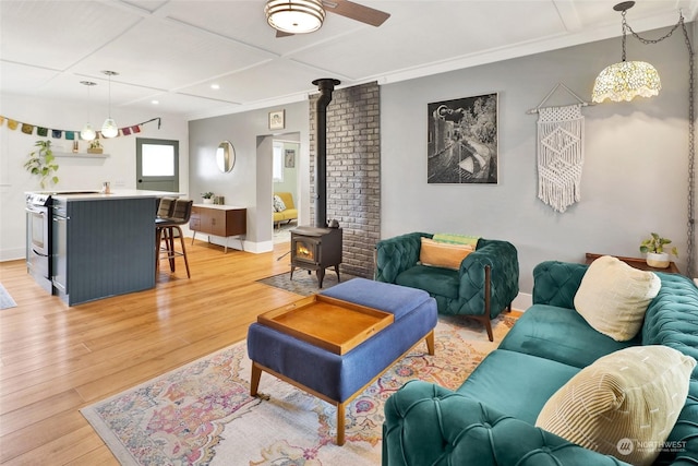 living room with a wood stove, ornamental molding, coffered ceiling, ceiling fan, and light hardwood / wood-style floors