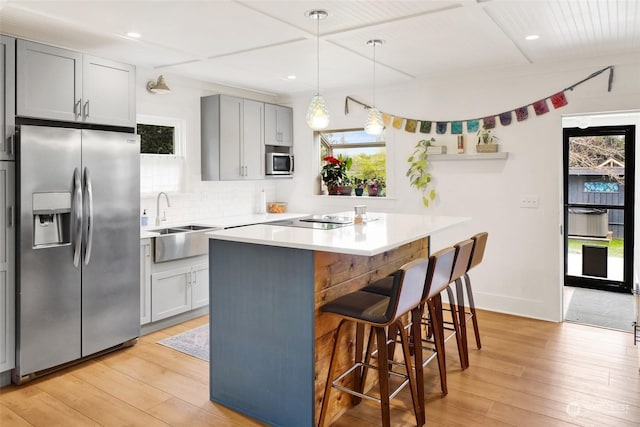 kitchen featuring gray cabinets, appliances with stainless steel finishes, a breakfast bar, sink, and a center island