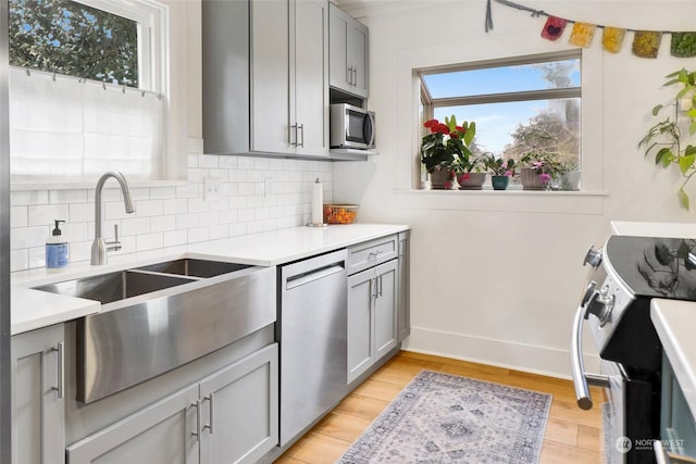 kitchen with gray cabinets, appliances with stainless steel finishes, sink, backsplash, and light hardwood / wood-style floors