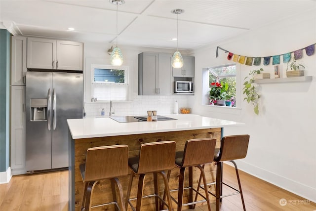 kitchen featuring gray cabinetry, backsplash, stainless steel appliances, a kitchen breakfast bar, and light wood-type flooring