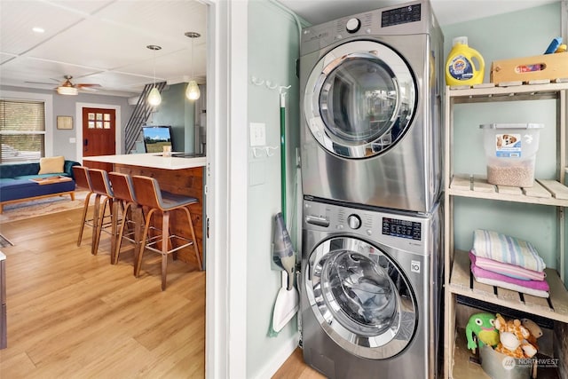 clothes washing area with light wood-type flooring, ceiling fan, and stacked washing maching and dryer